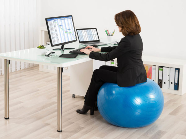 青年女商人坐在Pilates球上办公